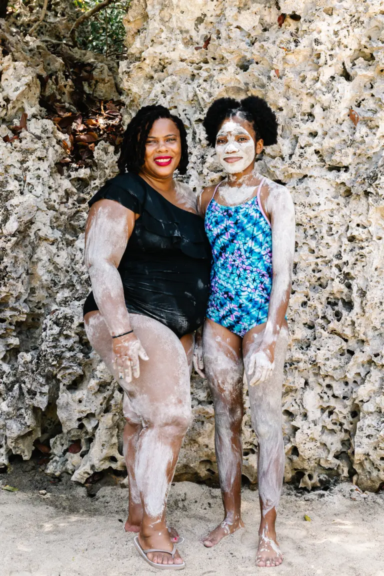 Two guests covered in mineral clay standing in front of the coral rock wall at the Nature Spa